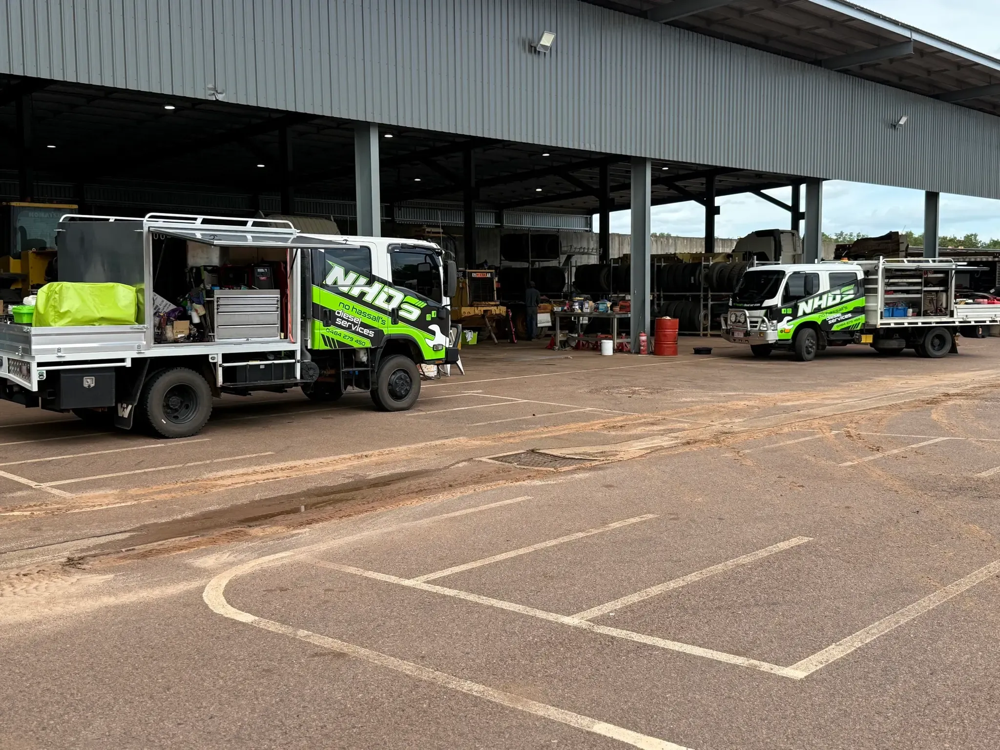 Two NHDS service trucks parked at a site workshop with plant under cover